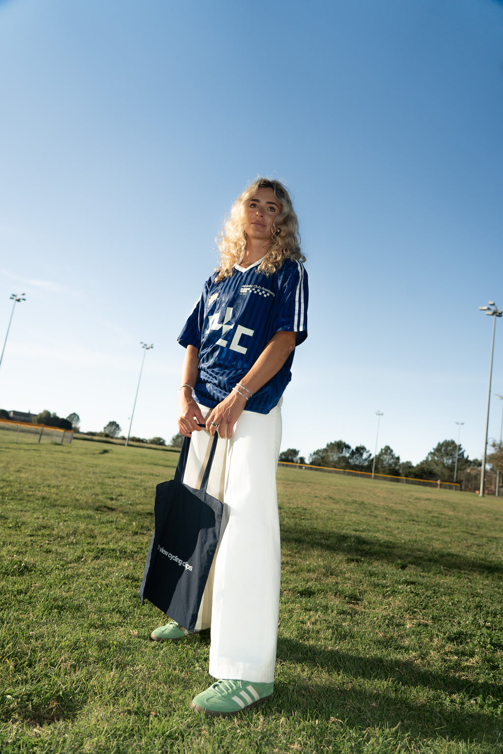 Person wearing a blue couch view jersey and white pants standing on a grassy field with a clear blue sky.