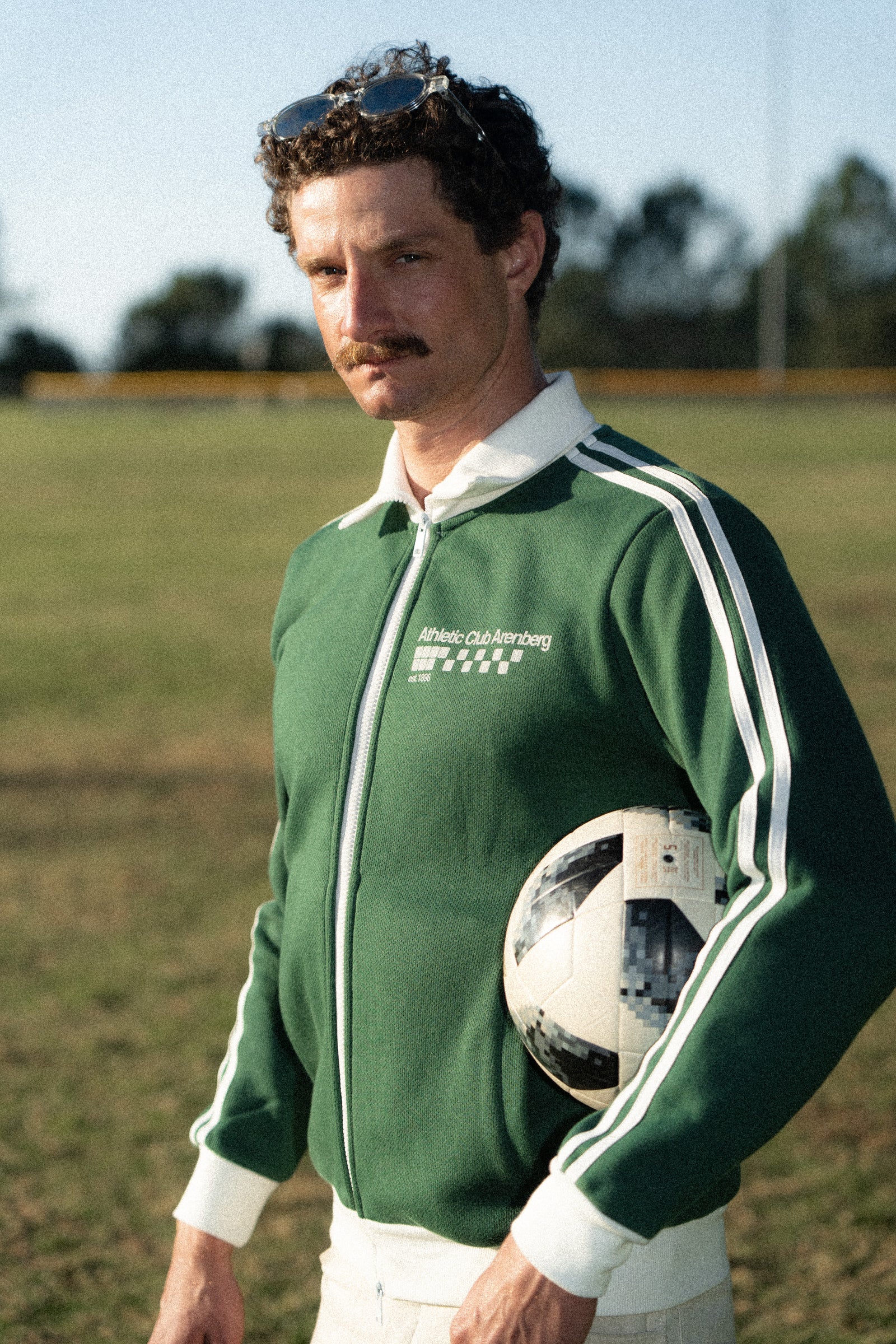 Man in a green tracksuit holding a soccer ball on a grassy field