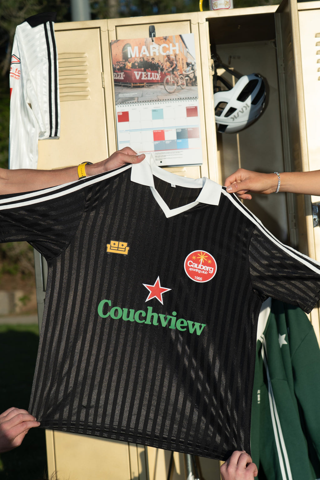 Person holding a black couch view jersey with visible branding in front of a locker.
