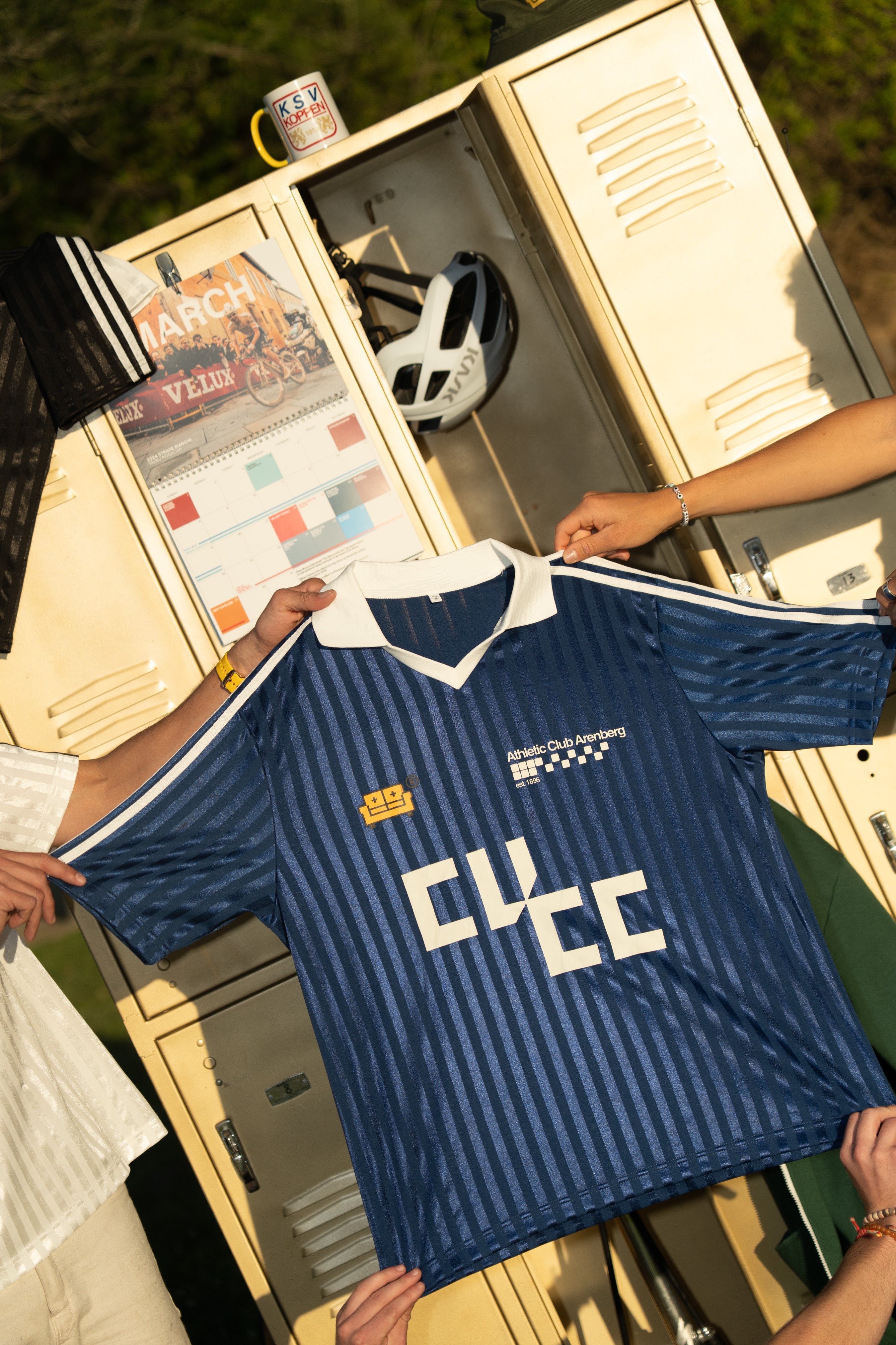 Person holding a blue couch view jersey with visible branding in front of an open locker containing cycling equipment.